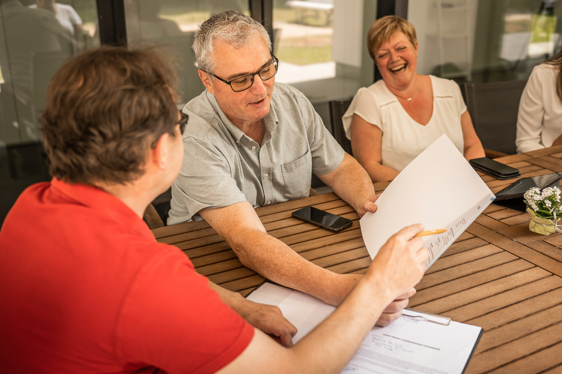 Drie mensen bespreken documenten aan een houten tafel tijdens een startersgesprek.